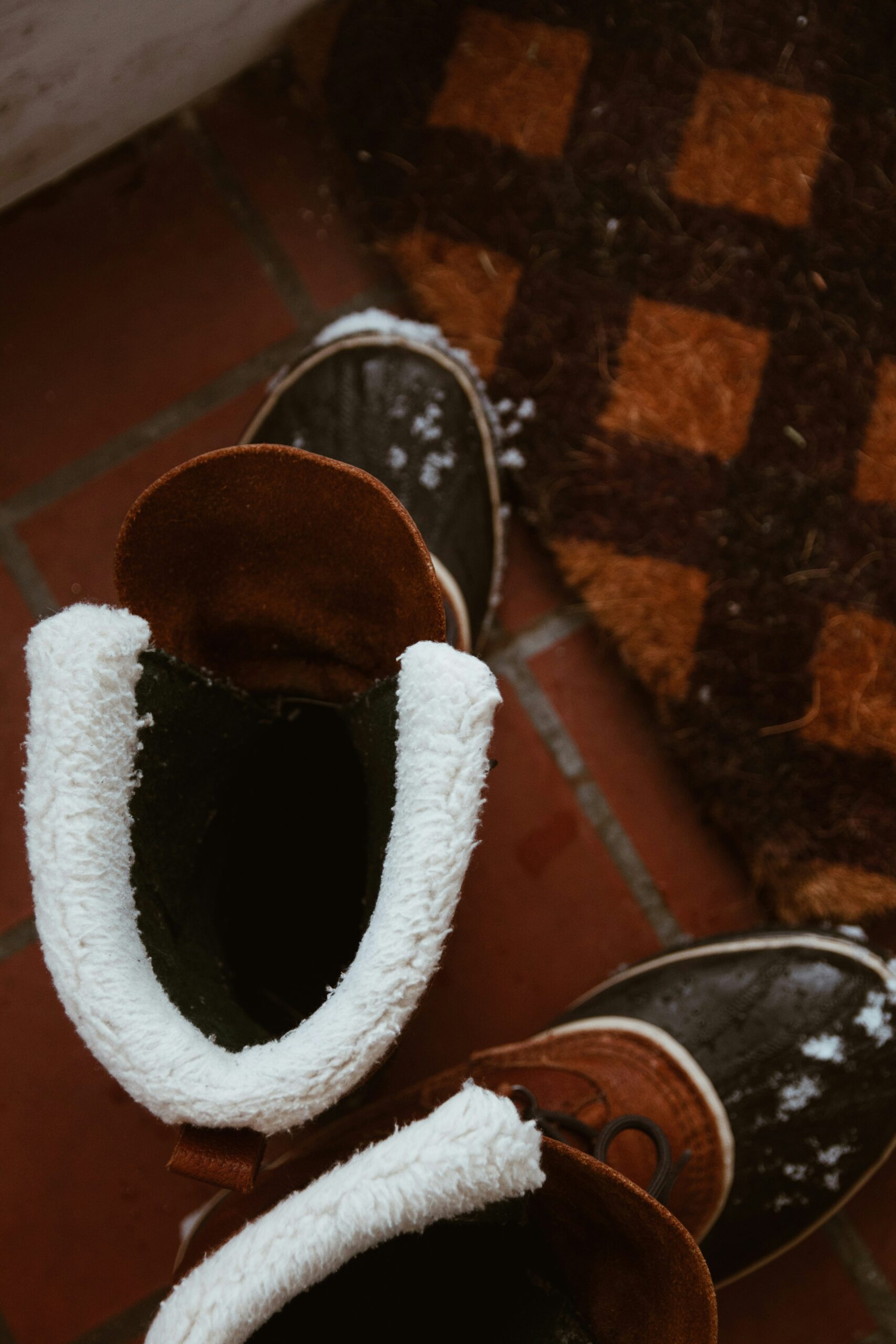 A first-person perspective looking down at tan leather lace-up work boots and blue jeans standing in deep, fresh white snow with visible footprints.